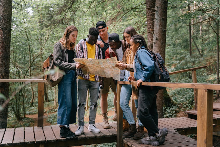 Group of young adults studying a map while hiking on a forest bridge.